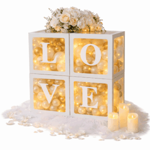 Dekoracyjne pudełka LOVE wypełnione złotymi i białymi balonikami, z delikatnym oświetleniem LED, tiulem, płatkami róż, świecami i bukietem kwiatów na górze.
