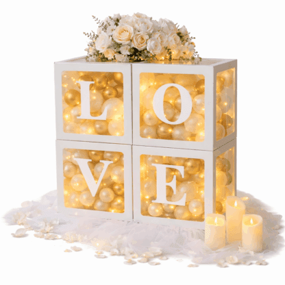 Dekoracyjne pudełka LOVE wypełnione złotymi i białymi balonikami, z delikatnym oświetleniem LED, tiulem, płatkami róż, świecami i bukietem kwiatów na górze.