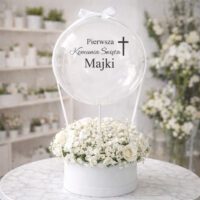 Naklejka na balon „Pierwsza Komunia Święta Majki” z krzyżem na przezroczystym balonie bubble w białym flowerboxie z kwiatami
